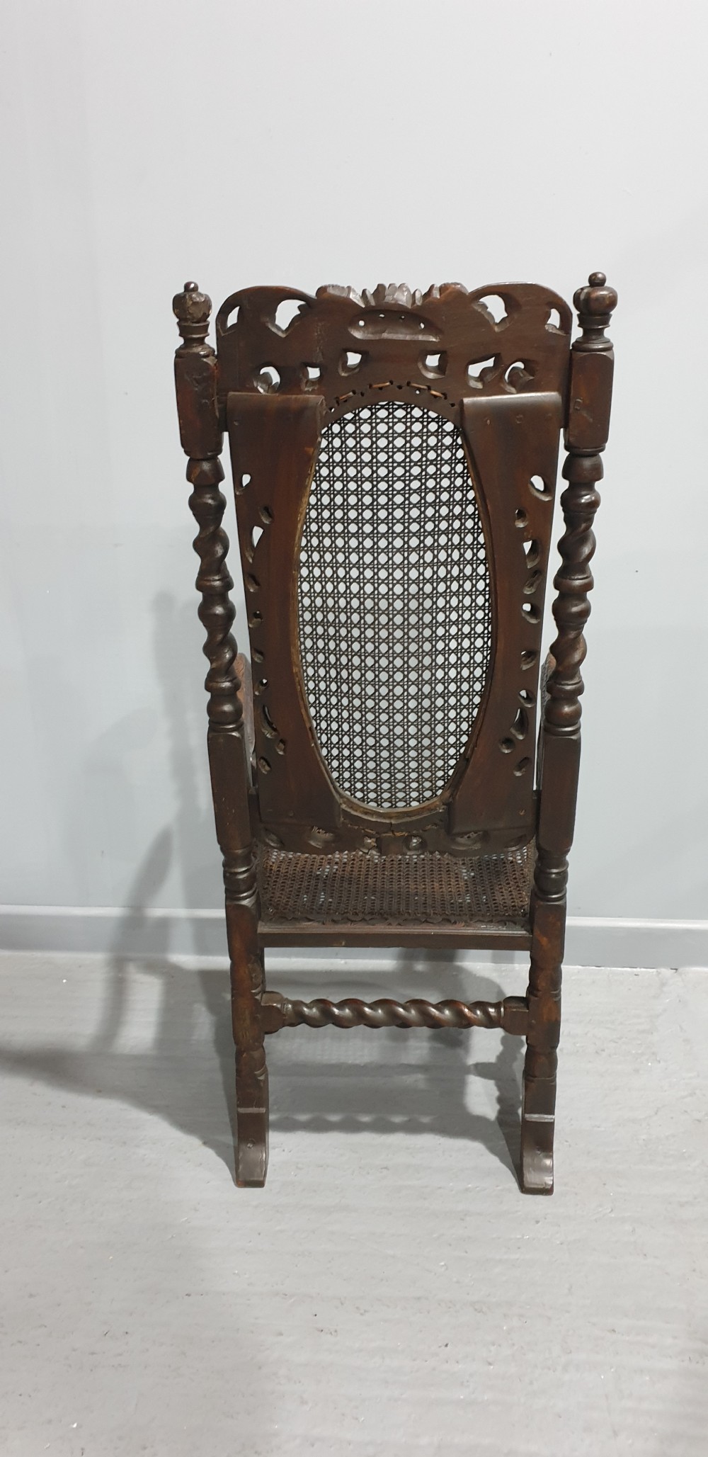 A high-backed dark oak carver chair featuring an oval cane backrest, barley twist posts, hand-carved cresting, and a patterned seat cushion. View XI