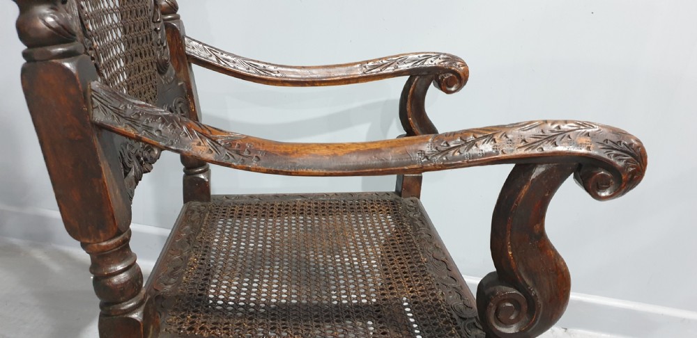 A high-backed dark oak carver chair featuring an oval cane backrest, barley twist posts, hand-carved cresting, and a patterned seat cushion. View XIV