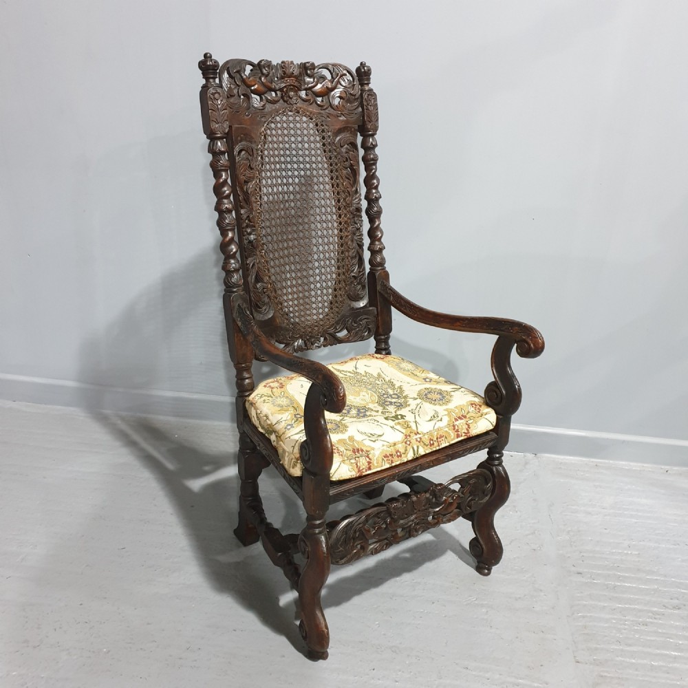 A high-backed dark oak carver chair featuring an oval cane backrest, barley twist posts, hand-carved cresting, and a patterned seat cushion.
