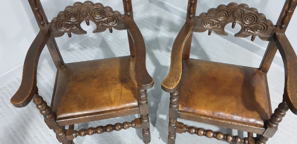 A pair of dark carved oak carver armchairs featuring decorative scrolled backrests, turned legs, bobbin stretchers, and leather seats. View III
