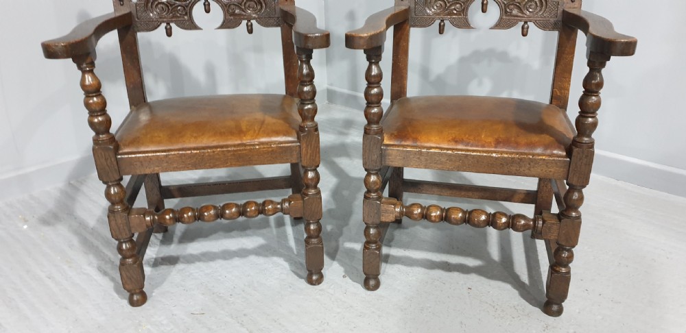 A pair of dark carved oak carver armchairs featuring decorative scrolled backrests, turned legs, bobbin stretchers, and leather seats. View IV