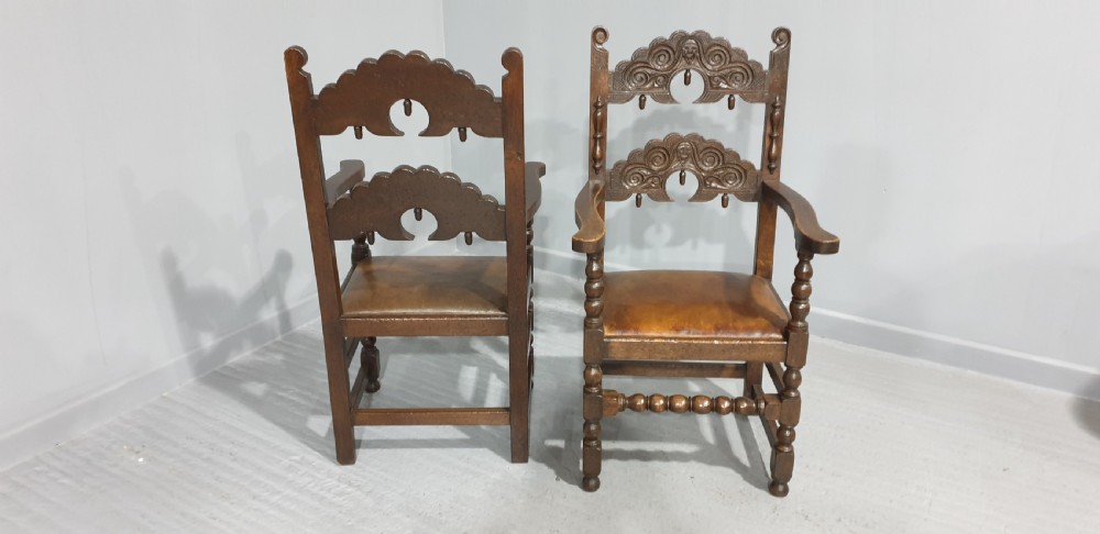 A pair of dark carved oak carver armchairs featuring decorative scrolled backrests, turned legs, bobbin stretchers, and leather seats. View VI