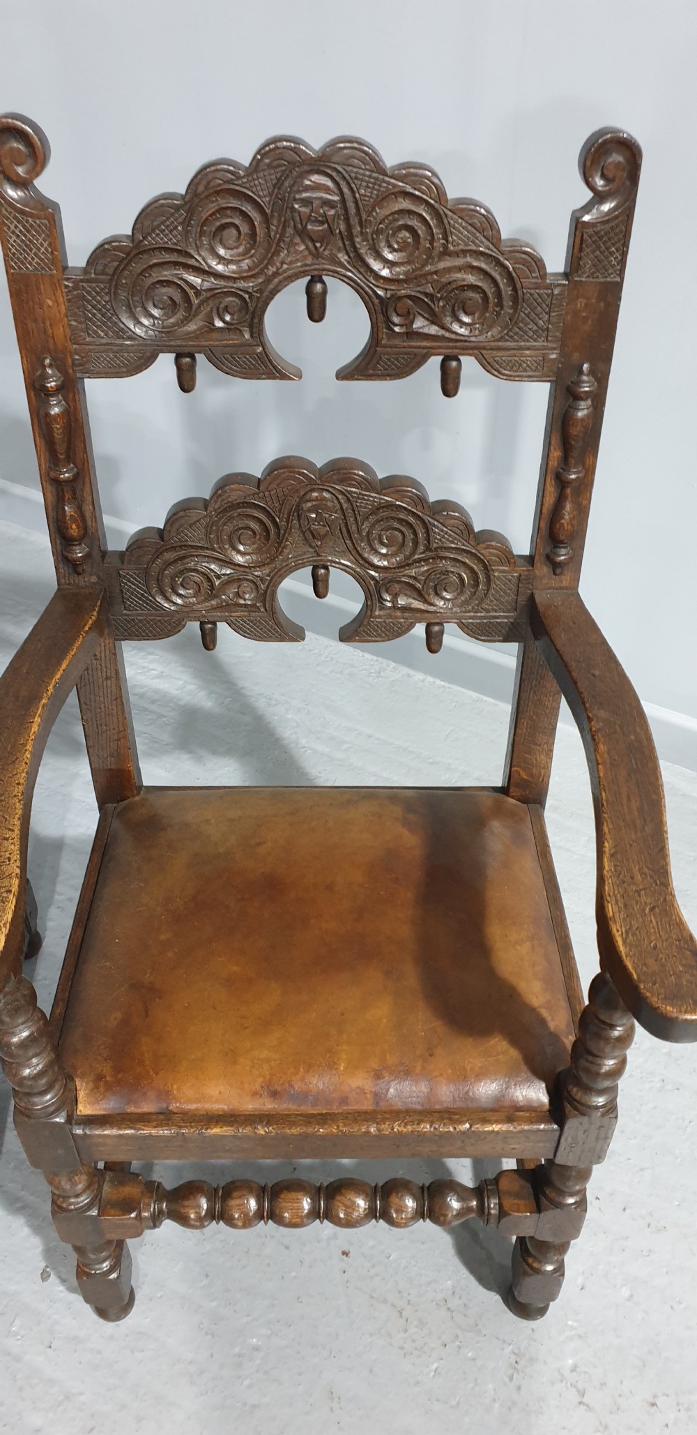 A pair of dark carved oak carver armchairs featuring decorative scrolled backrests, turned legs, bobbin stretchers, and leather seats. View VII
