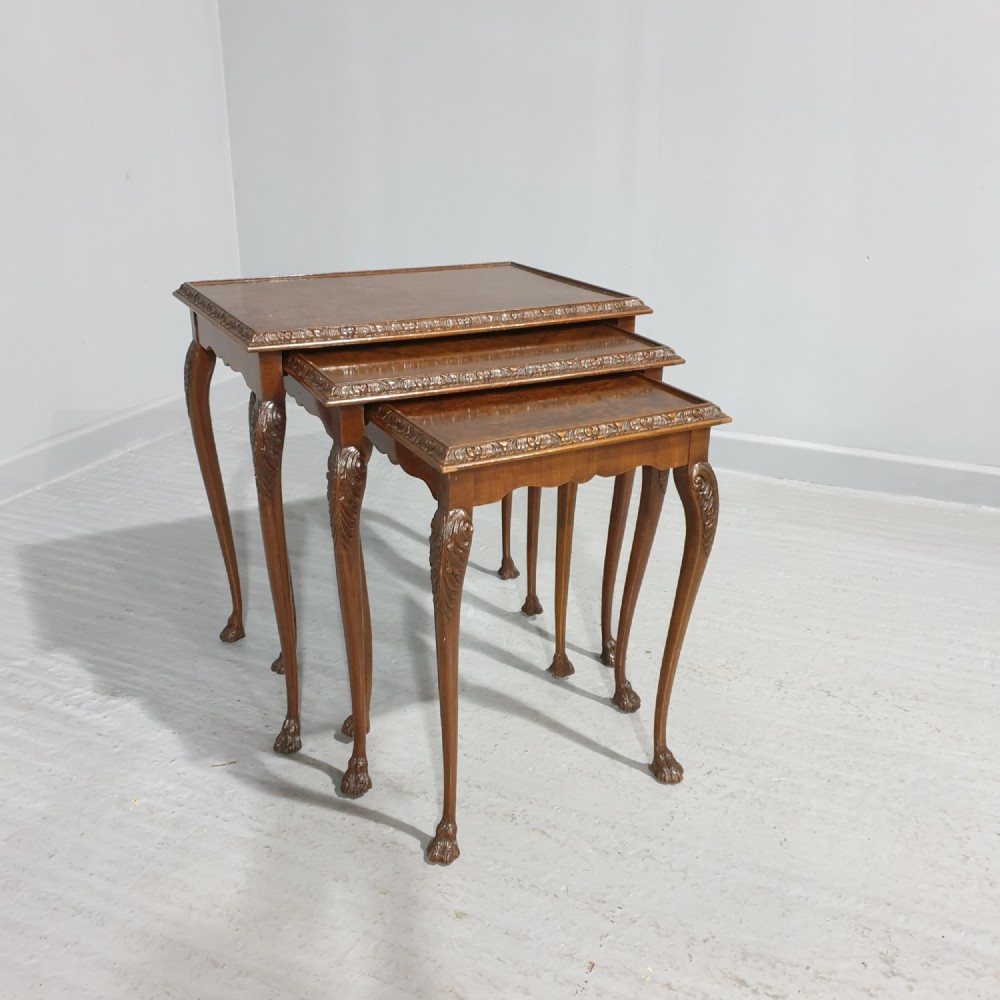 A set of three graduated burr walnut nesting tables with carved borders, cabriole legs, and claw and ball feet.