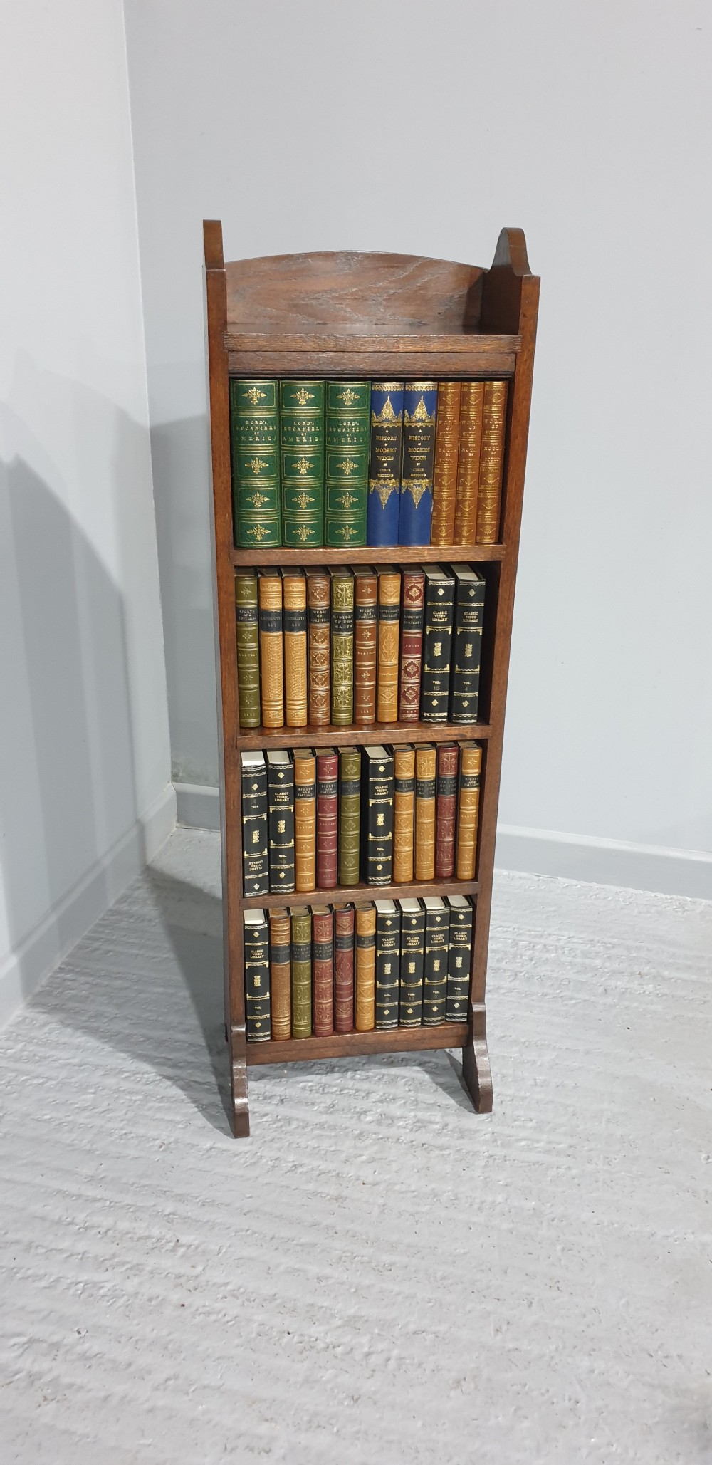 A tall, narrow open oak bookcase featuring four fixed shelves and shaped side panels standing on bracket feet. View II
