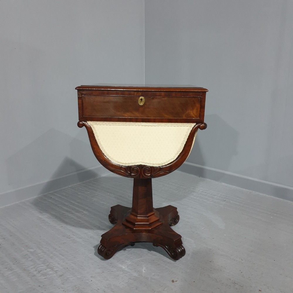 A William IV mahogany work box table featuring a single drawer over a cream fabric-lined storage well, supported on a central pedestal and quadform base with scroll feet.