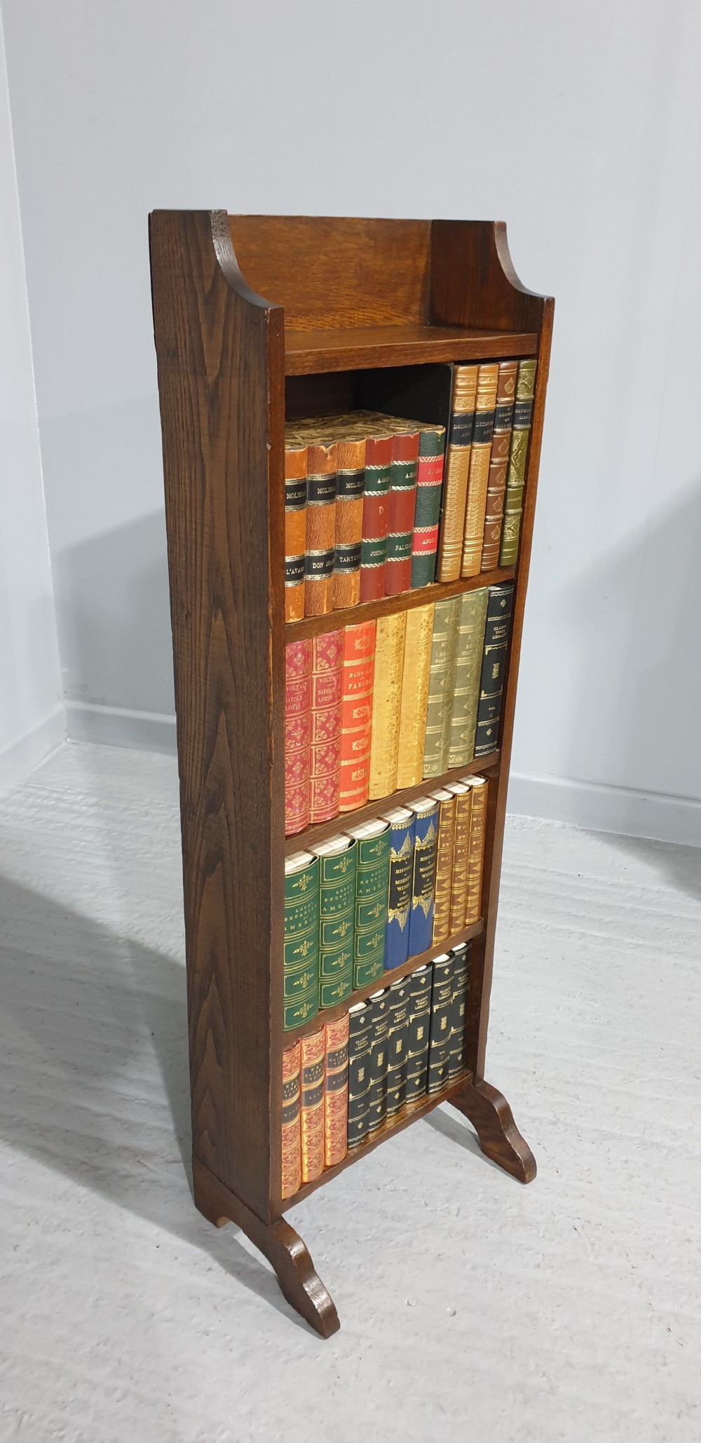 A slim floor-standing solid oak open bookcase featuring four tiered shelves filled with colourful antique books. View II