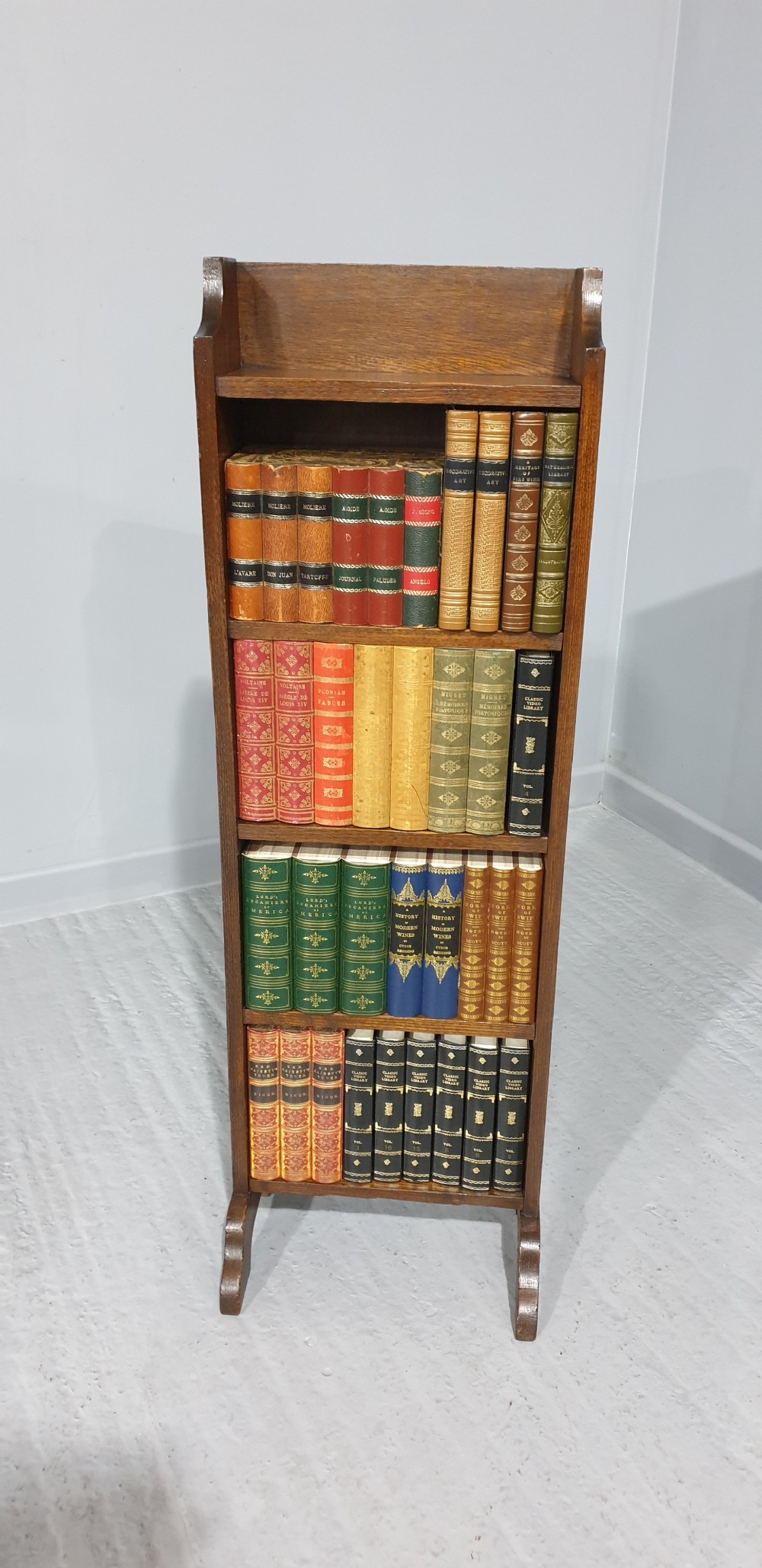 A slim floor-standing solid oak open bookcase featuring four tiered shelves filled with colourful antique books. View III