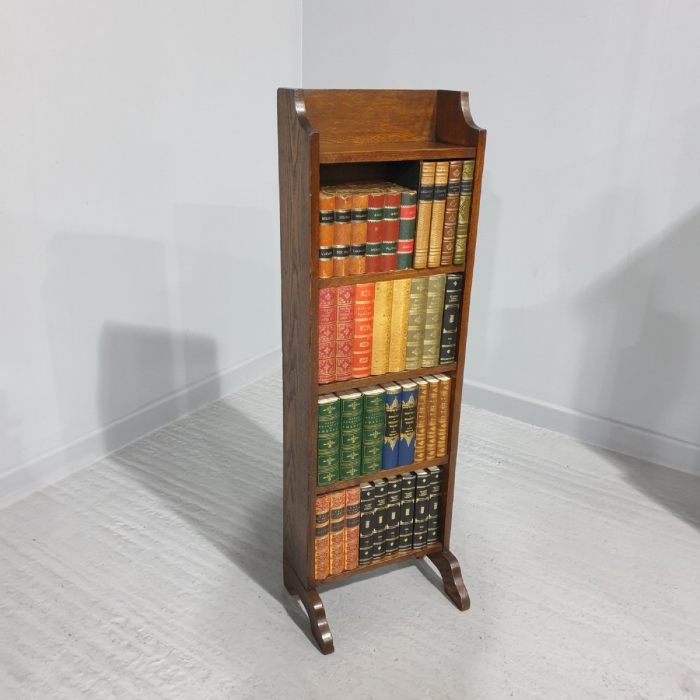 A slim floor-standing solid oak open bookcase featuring four tiered shelves filled with colourful antique books.