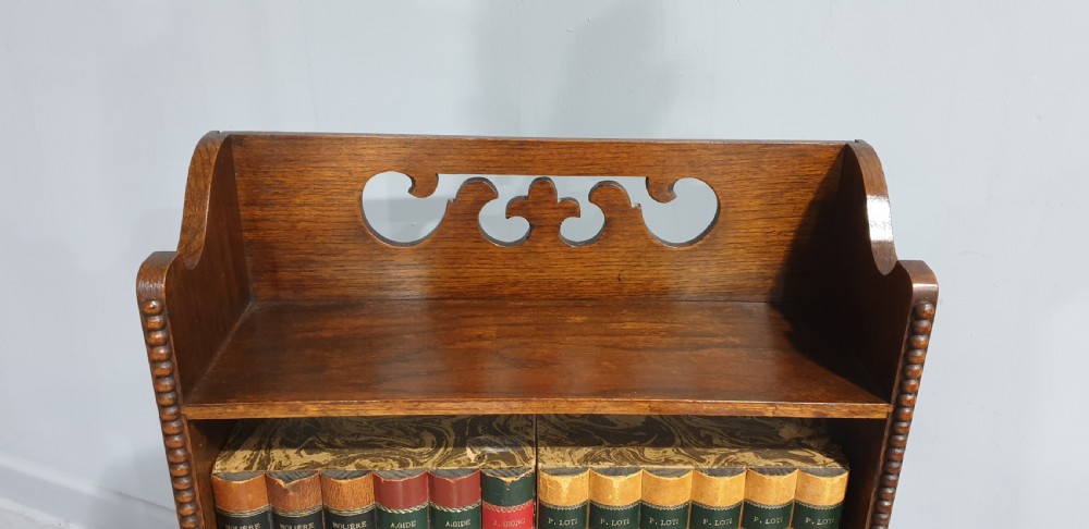 A slim freestanding open oak bookcase with three shelves, bobbin turned edge moulding, and a carved cresting top gallery rail. View II