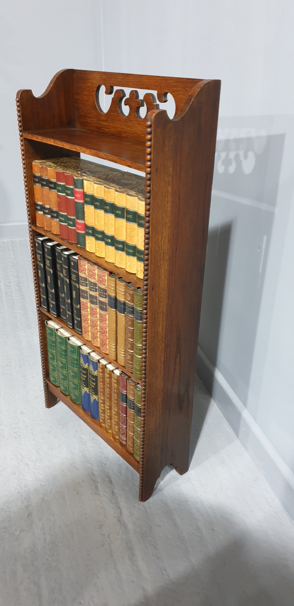 A slim freestanding open oak bookcase with three shelves, bobbin turned edge moulding, and a carved cresting top gallery rail. View III