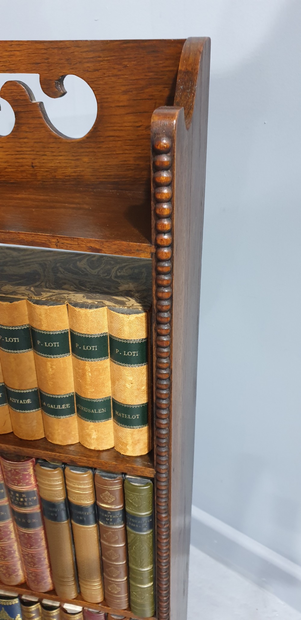 A slim freestanding open oak bookcase with three shelves, bobbin turned edge moulding, and a carved cresting top gallery rail. View V