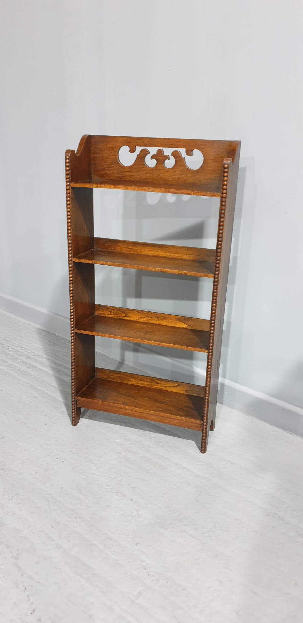A slim freestanding open oak bookcase with three shelves, bobbin turned edge moulding, and a carved cresting top gallery rail. View VI