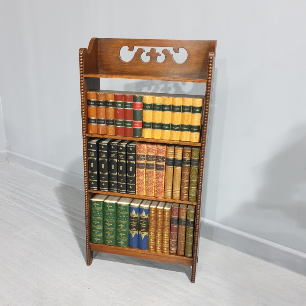 A slim freestanding open oak bookcase with three shelves, bobbin turned edge moulding, and a carved cresting top gallery rail.