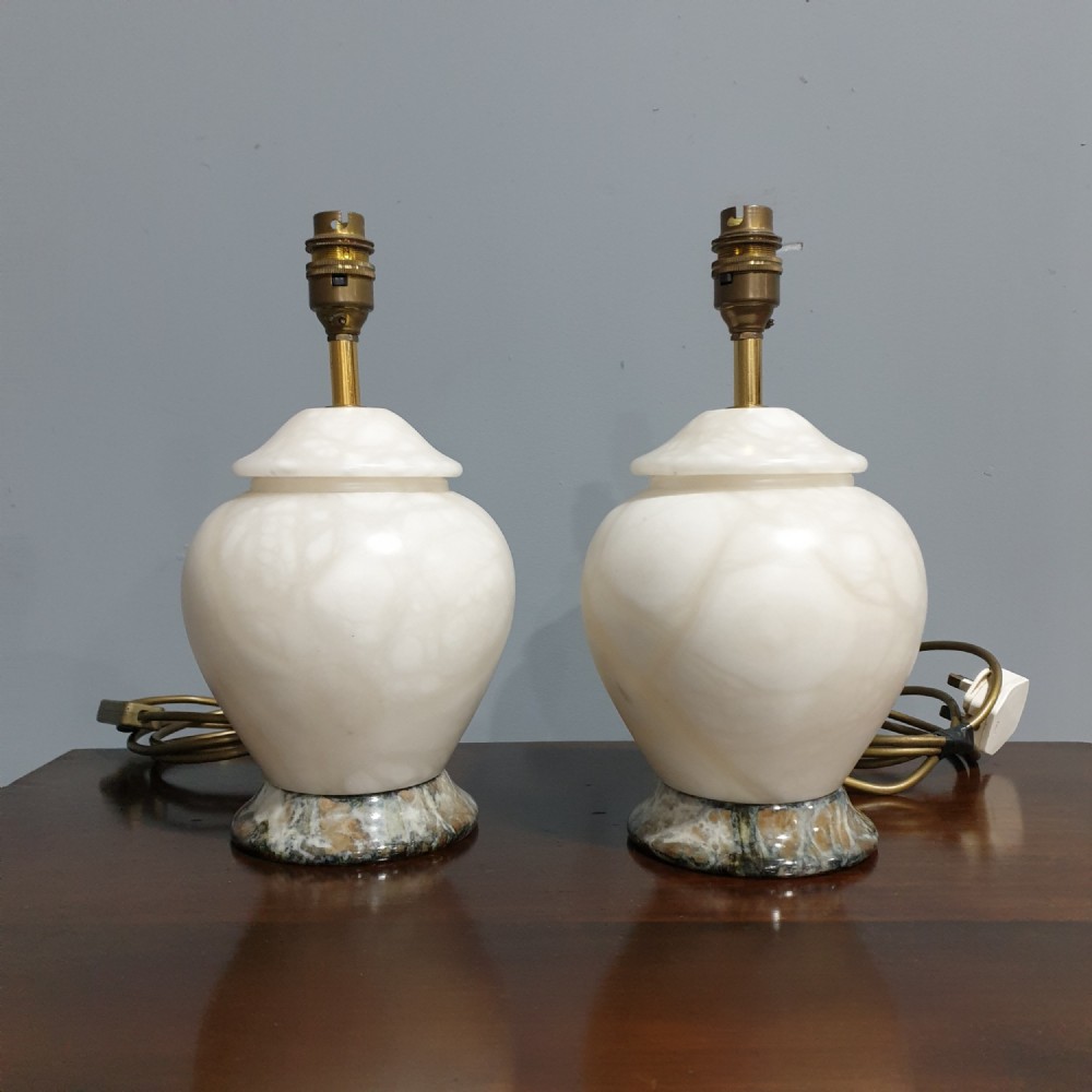 A pair of urn-shaped cream alabaster table lamps with variegated grey marble bases and brass fittings.