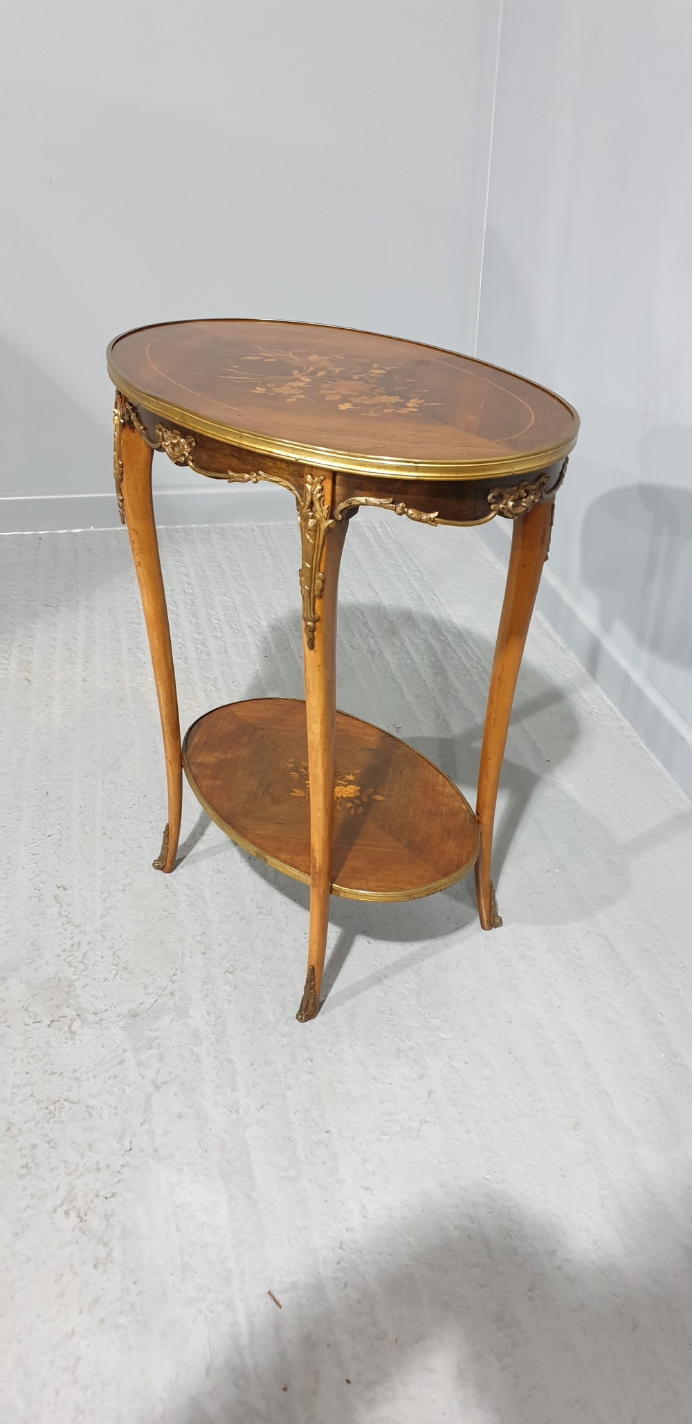 An oval French-style two-tier occasional table featuring floral marquetry inlay, slender cabriole legs, and gilt-bronze mounts. View VIII