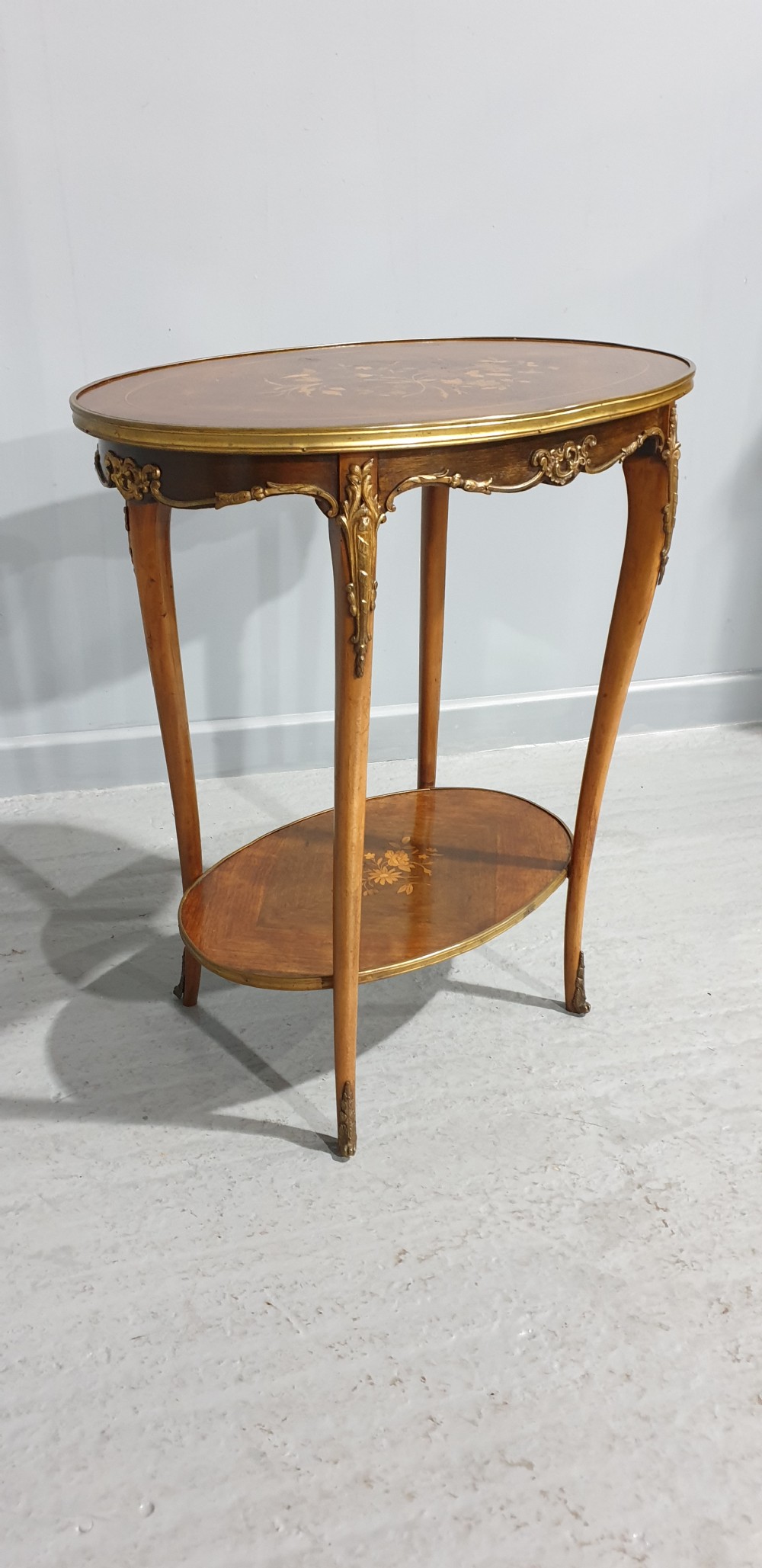 An oval French-style two-tier occasional table featuring floral marquetry inlay, slender cabriole legs, and gilt-bronze mounts. View X