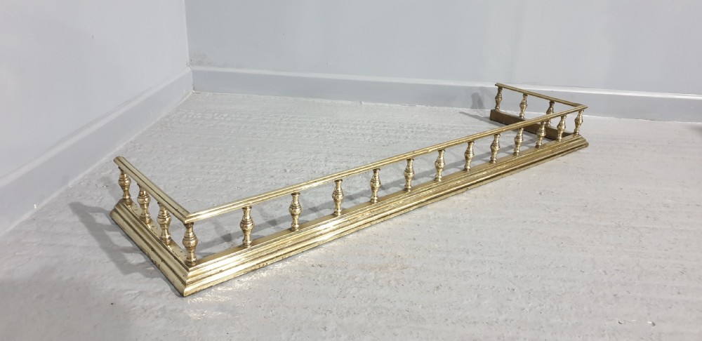 An antique Victorian brass fireplace fender featuring a low gallery with turned balusters along a stepped base.