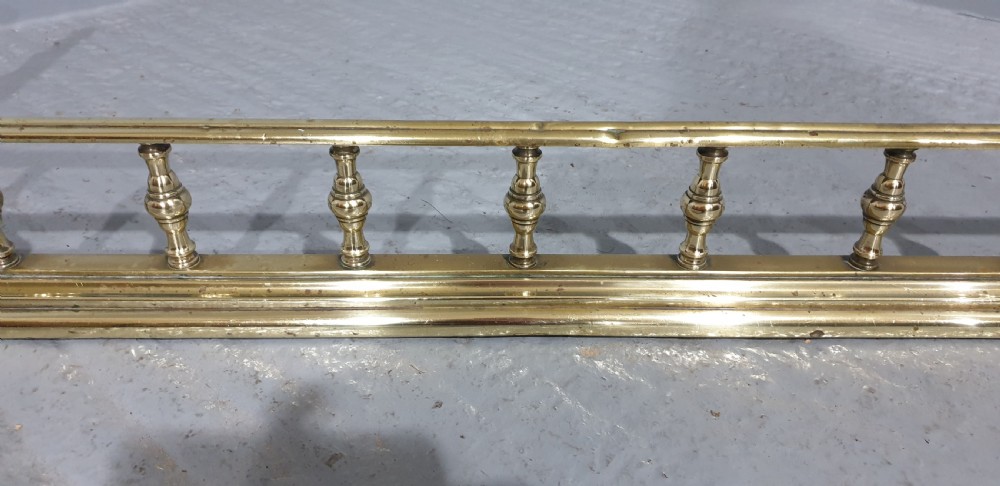 An antique Victorian brass fireplace fender featuring a low gallery with turned balusters along a stepped base. View III
