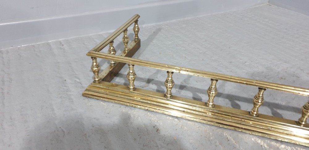 An antique Victorian brass fireplace fender featuring a low gallery with turned balusters along a stepped base. View IV