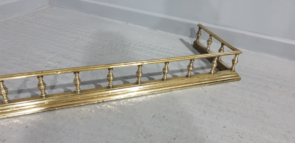An antique Victorian brass fireplace fender featuring a low gallery with turned balusters along a stepped base. View V