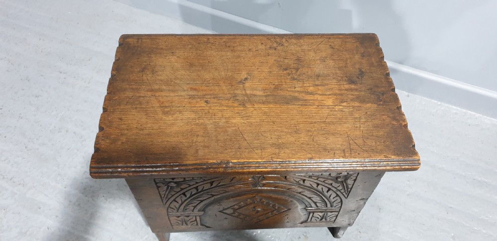 A small dark oak coffer featuring detailed arcaded and lozenge carved motifs on the front panel. View VII