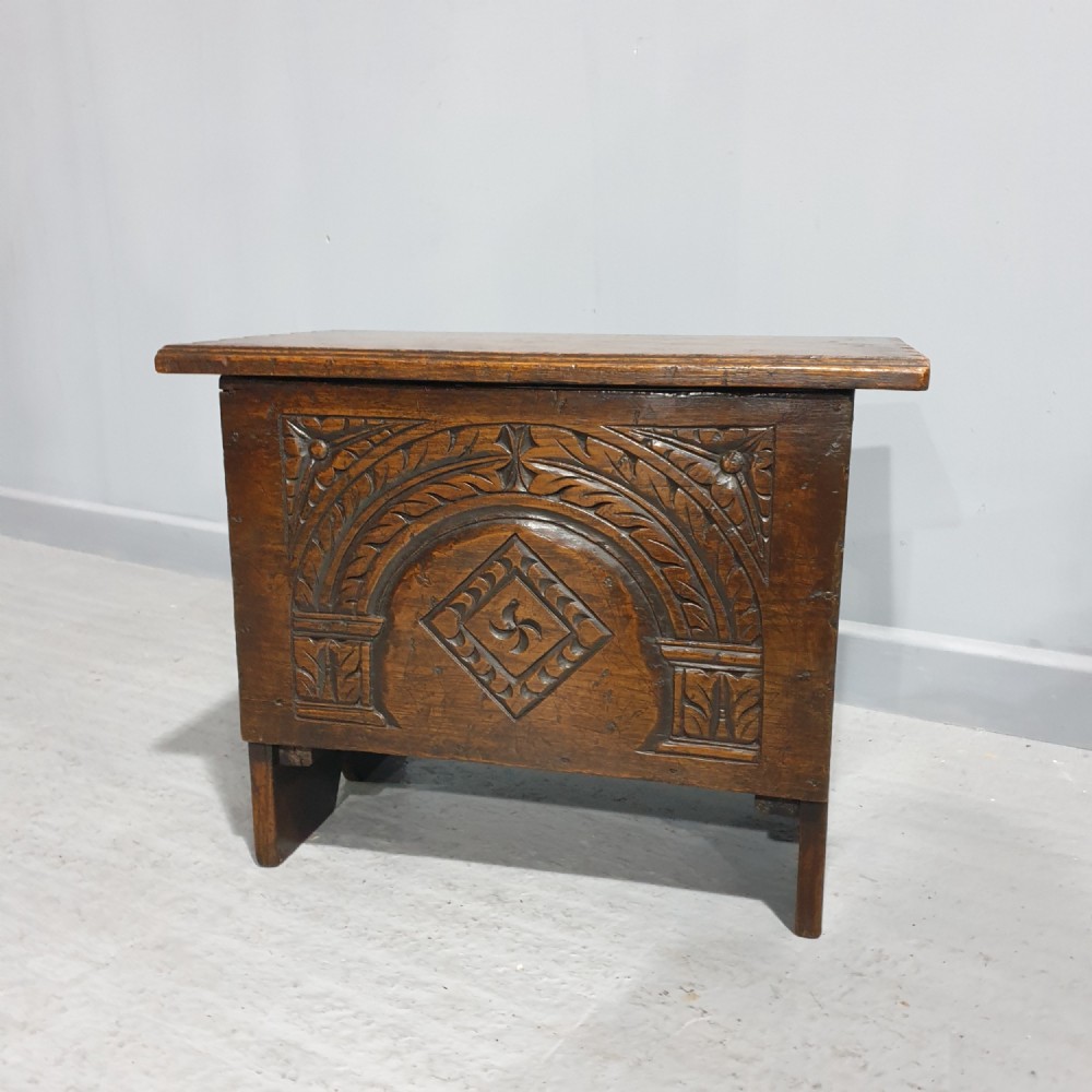 A small dark oak coffer featuring detailed arcaded and lozenge carved motifs on the front panel.