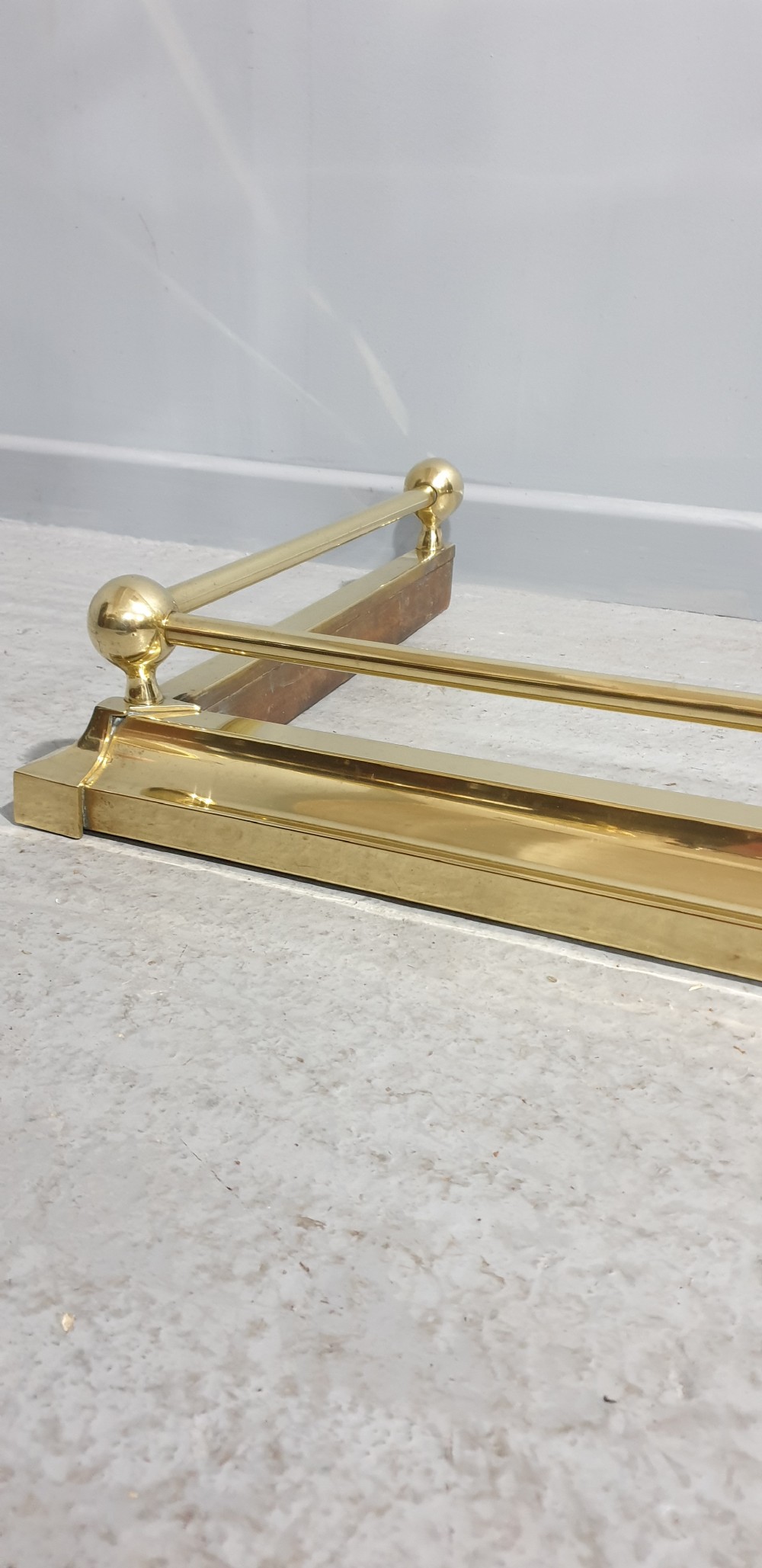 A polished Victorian brass fireplace fender featuring tubular upper rails and spherical corner finials set on a stepped base. View II