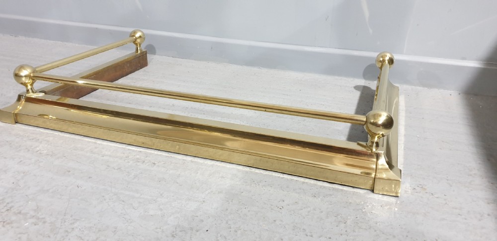 A polished Victorian brass fireplace fender featuring tubular upper rails and spherical corner finials set on a stepped base. View III