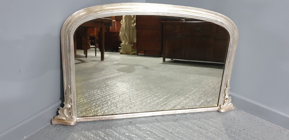 A Victorian silvered overmantel mirror featuring an arched top and moulded scroll feet at the base. View IV