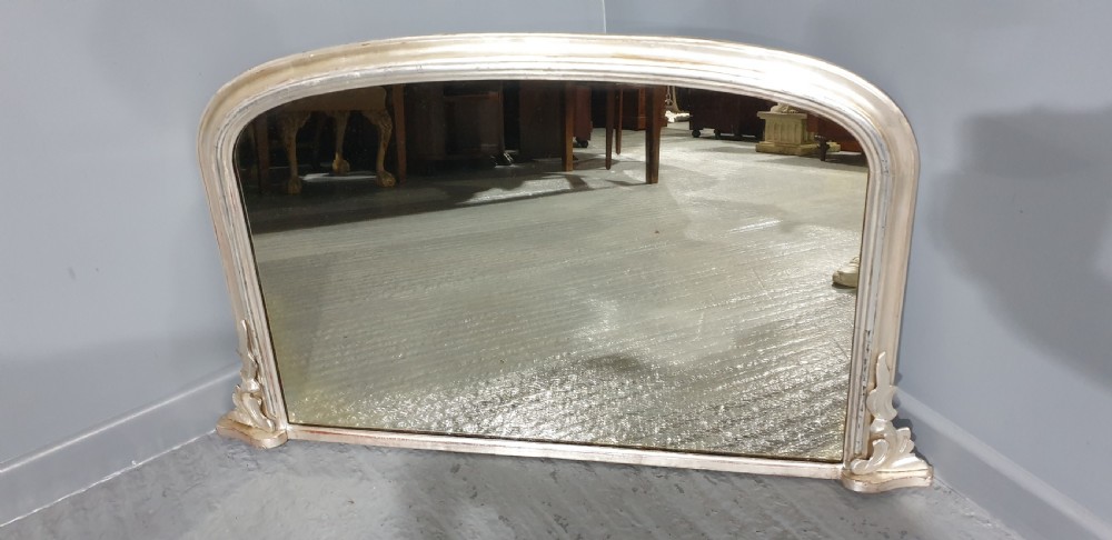 A Victorian silvered overmantel mirror featuring an arched top and moulded scroll feet at the base. View VI