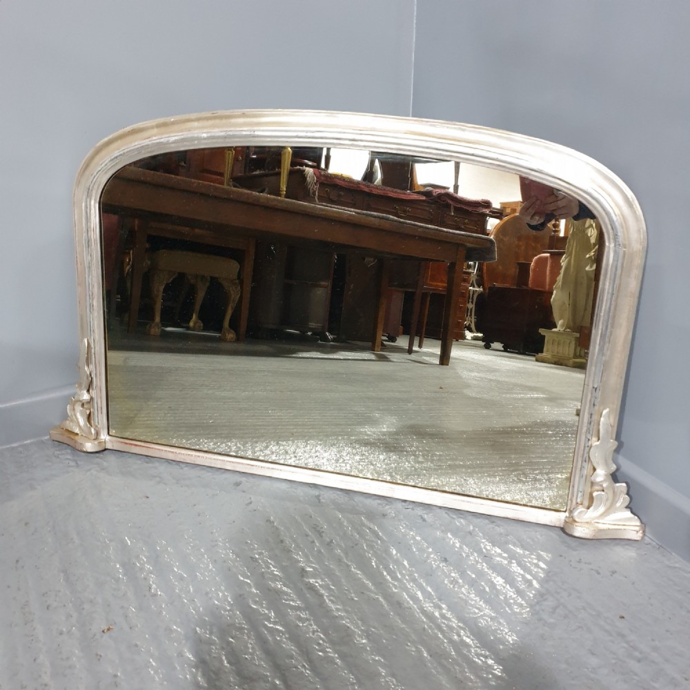 A Victorian silvered overmantel mirror featuring an arched top and moulded scroll feet at the base.