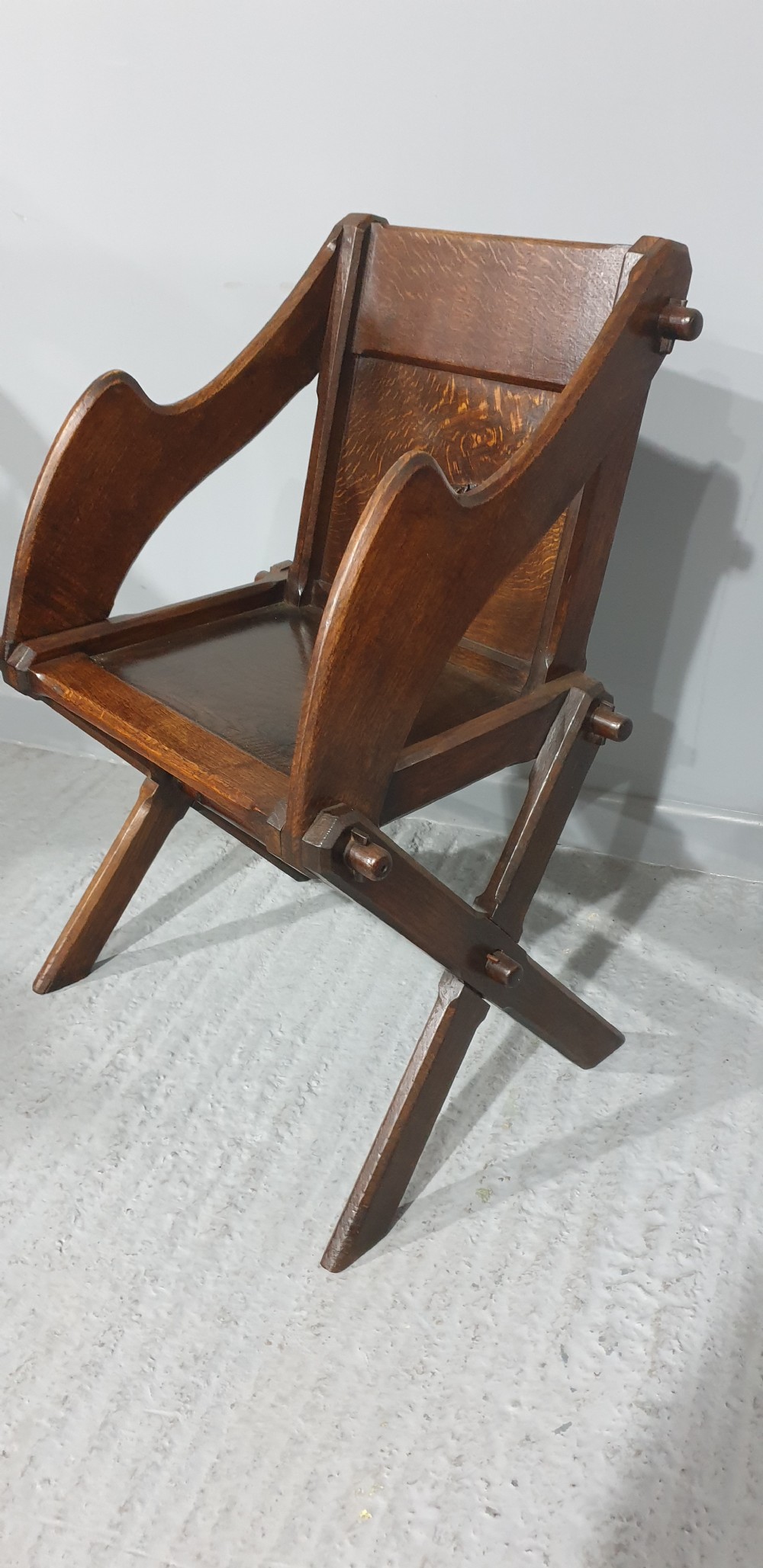 A Victorian dark oak Glastonbury chair with an X-frame base, shaped armrests, and a carved central leaf motif on the panelled back. View IV