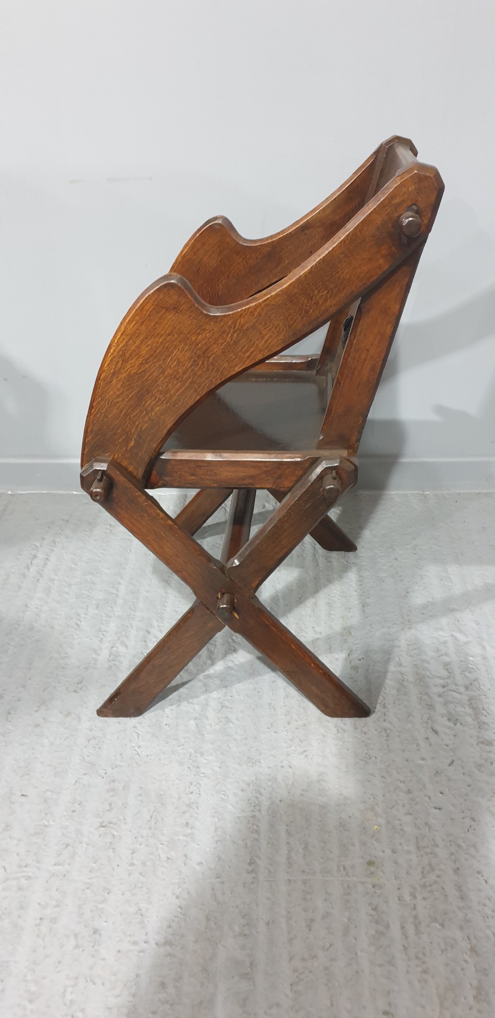 A Victorian dark oak Glastonbury chair with an X-frame base, shaped armrests, and a carved central leaf motif on the panelled back. View V