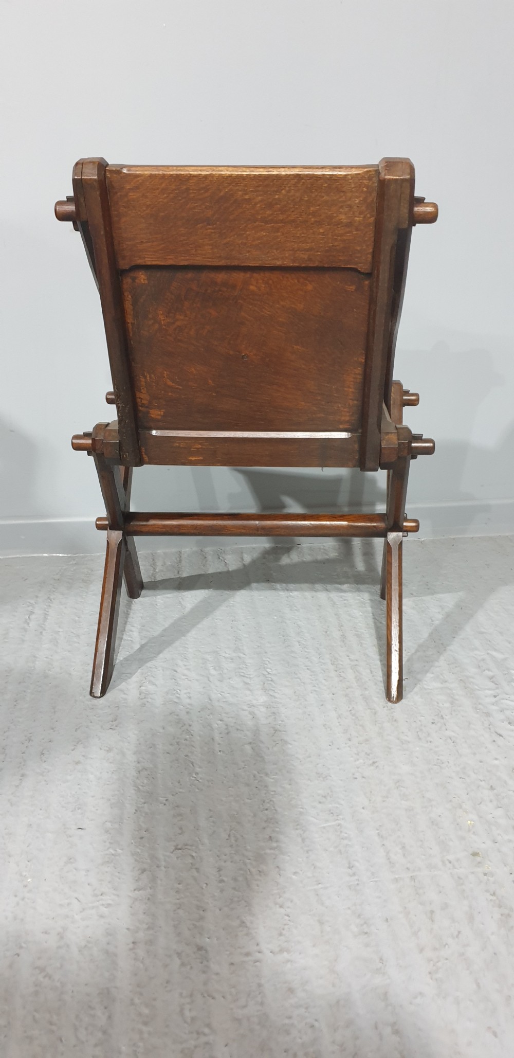 A Victorian dark oak Glastonbury chair with an X-frame base, shaped armrests, and a carved central leaf motif on the panelled back. View VI