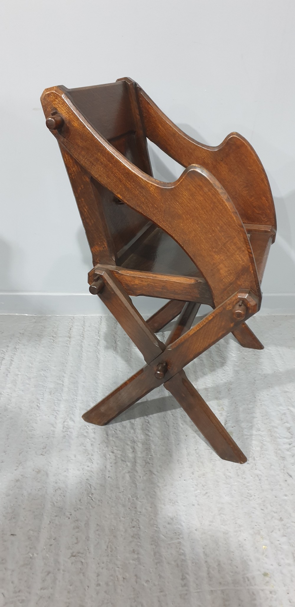 A Victorian dark oak Glastonbury chair with an X-frame base, shaped armrests, and a carved central leaf motif on the panelled back. View VII