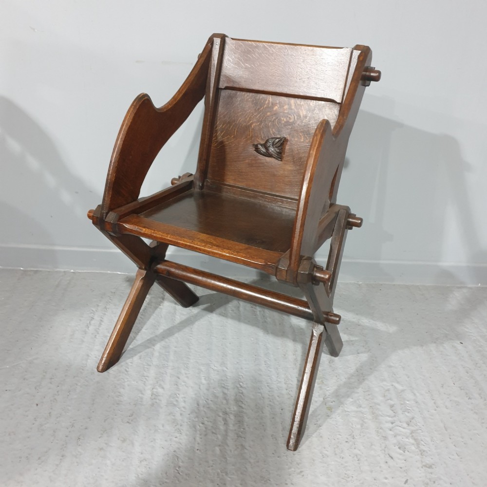 A Victorian dark oak Glastonbury chair with an X-frame base, shaped armrests, and a carved central leaf motif on the panelled back.