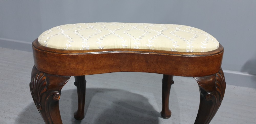 A Victorian kidney-shaped stool crafted from burr walnut featuring carved cabriole legs and cream patterned upholstery. View V