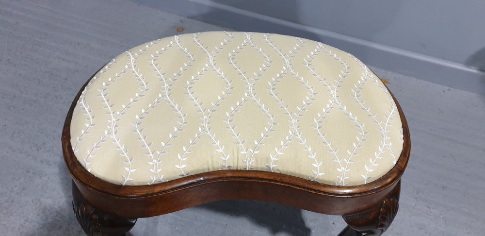 A Victorian kidney-shaped stool crafted from burr walnut featuring carved cabriole legs and cream patterned upholstery. View VII