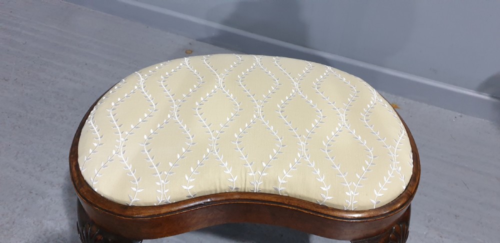 A Victorian kidney-shaped stool crafted from burr walnut featuring carved cabriole legs and cream patterned upholstery. View VIII
