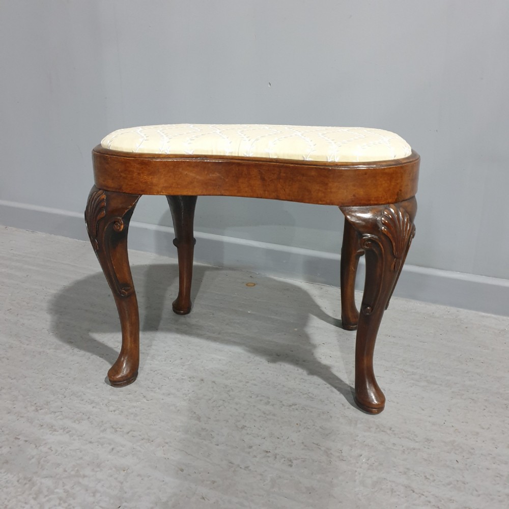 A Victorian kidney-shaped stool crafted from burr walnut featuring carved cabriole legs and cream patterned upholstery.