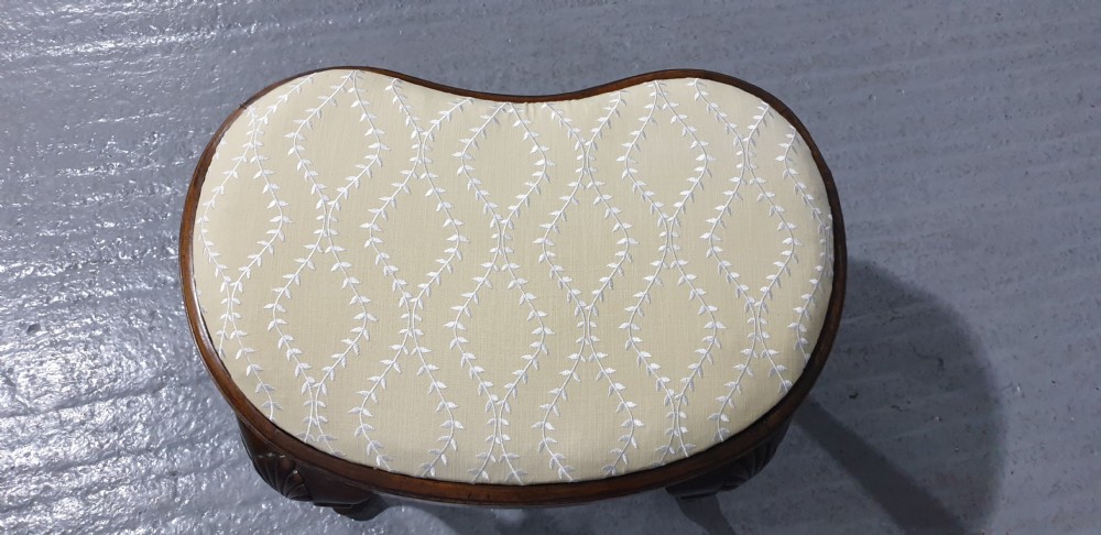 A Victorian kidney-shaped stool crafted from burr walnut featuring carved cabriole legs and cream patterned upholstery. View VI