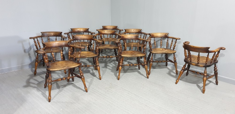 A set of ten antique English elm smokers bow armchairs featuring horseshoe crest rails, turned spindles, shaped saddle seats, and turned legs. View VII