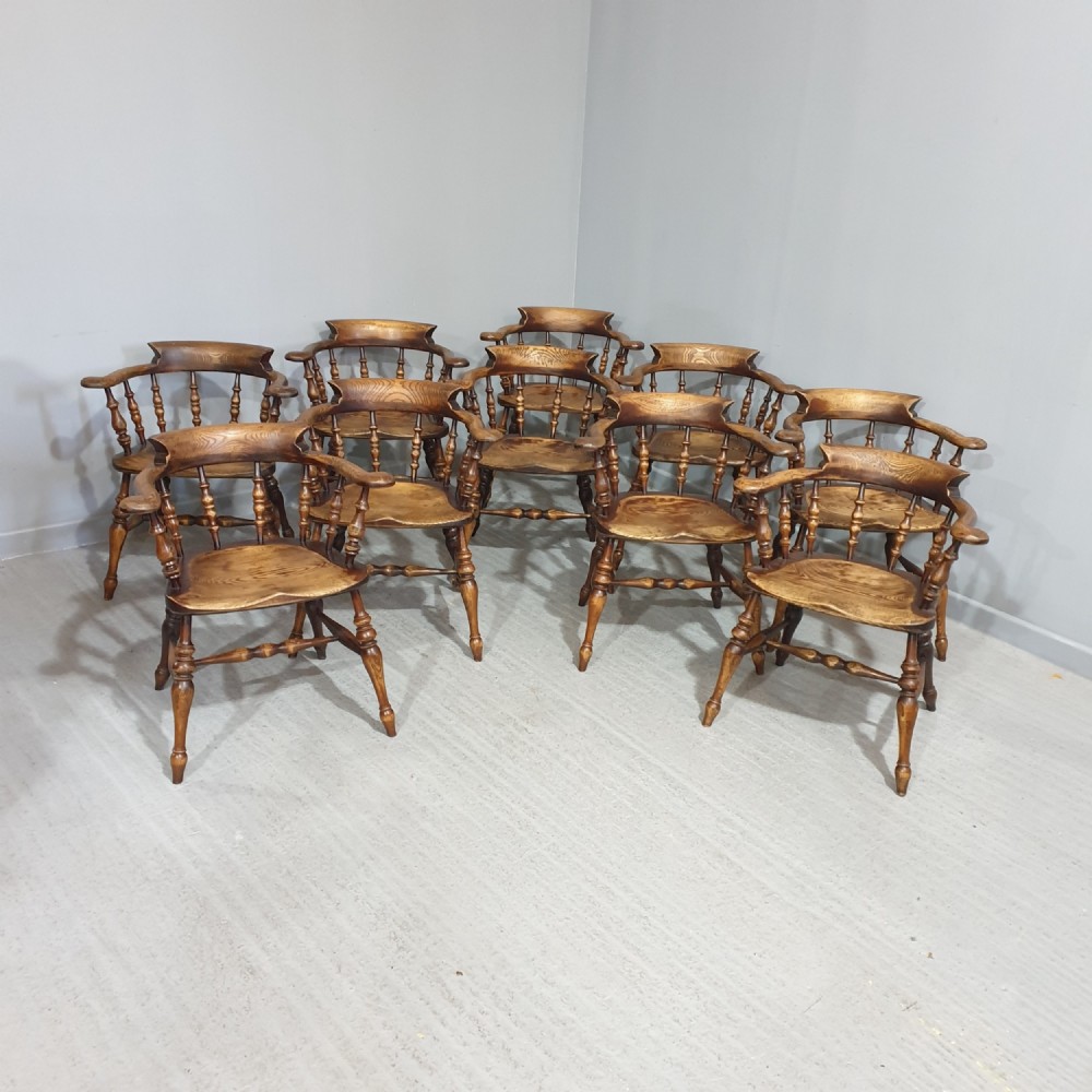 A set of ten antique English elm smokers bow armchairs featuring horseshoe crest rails, turned spindles, shaped saddle seats, and turned legs.