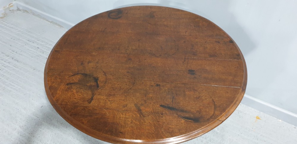 A Georgian period circular oak table shown with its tilt-top surface hinged vertically above a central turned pillar and three splayed cabriole legs. View VI