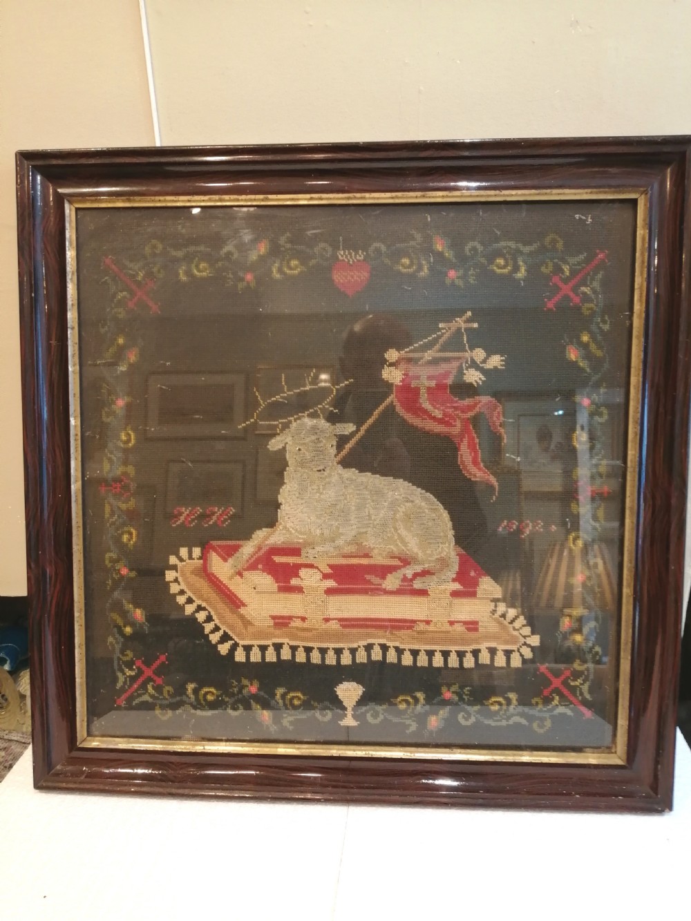 An early nineteenth-century framed raised woolwork picture depicting the Agnus Dei resting on a red book within a floral border. View V