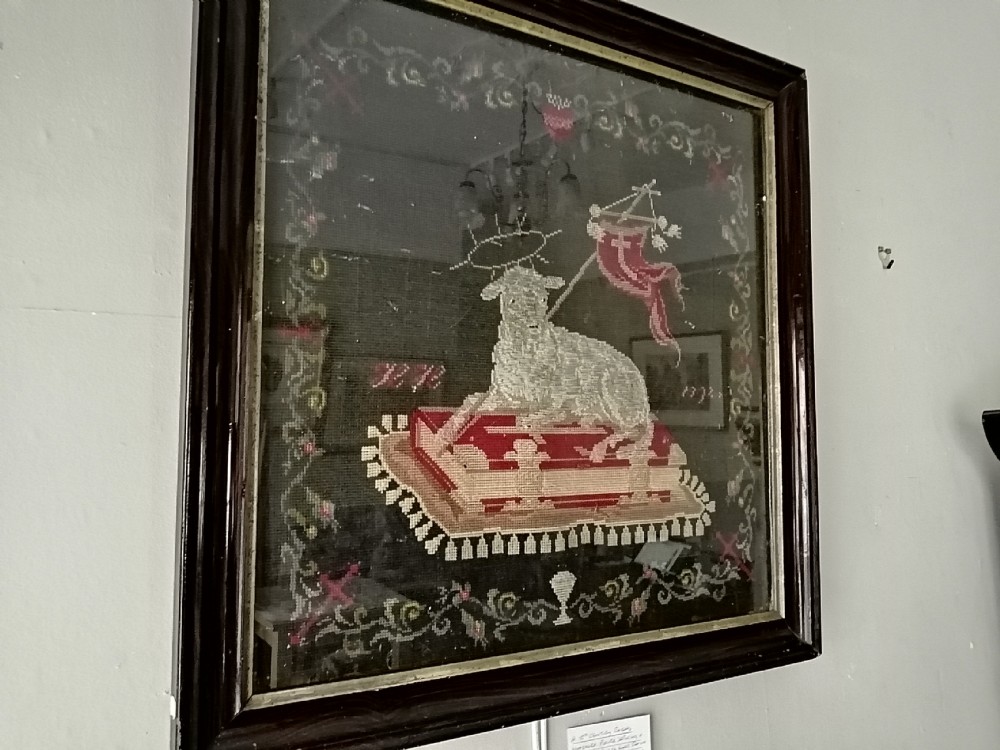 An early nineteenth-century framed raised woolwork picture depicting the Agnus Dei resting on a red book within a floral border.