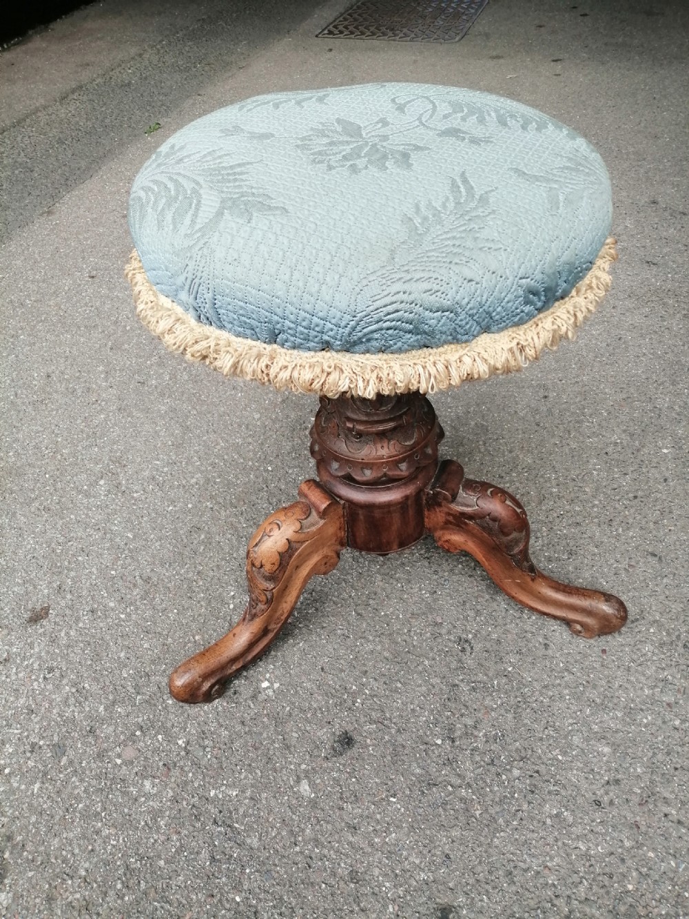 A 19th-century Victorian walnut rise and fall piano stool featuring a circular light blue patterned upholstered seat with fringed trim set on a carved tripod base.