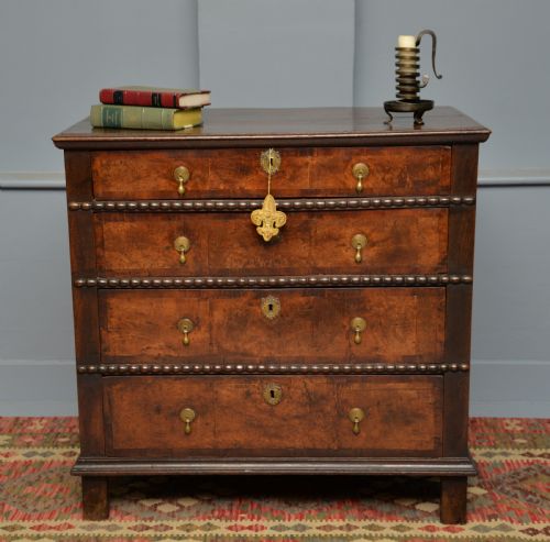 fig 1. A William and Mary walnut and yew wood chest of four drawers featuring brass teardrop handles and decorative bead moulding.