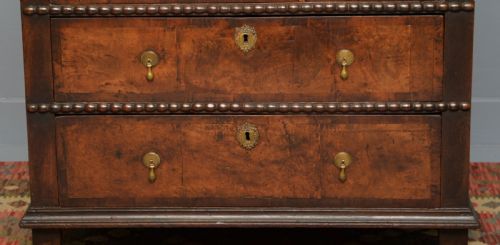 fig 3. A William and Mary walnut and yew wood chest of four drawers featuring brass teardrop handles and decorative bead moulding.